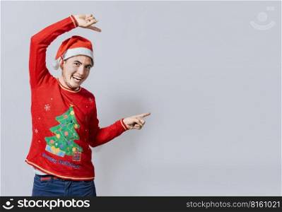 Friendly Christmas man pointing to a space to the side. Friendly smiling young man in christmas clothes pointing at a promo, Cheerful christmas man concept pointing promo offer isolated