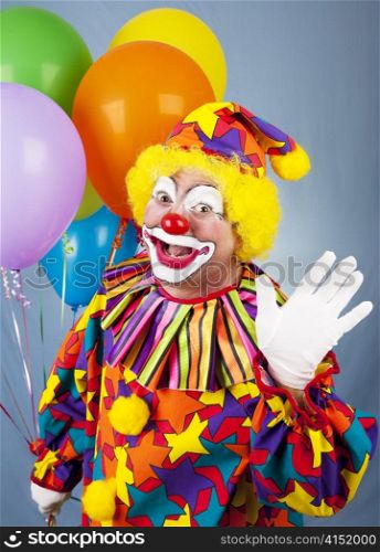 Friendly circus clown holding a bunch of balloons and waving hello.