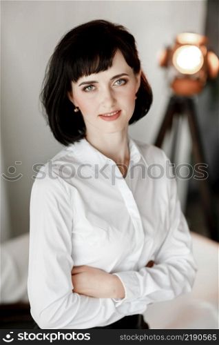 Friendly confident young woman with folded arms smiling at the camera. Girl in white shirt and leather skirt sitting at home studio.. Friendly confident young woman with folded arms smiling at the camera. Girl in white shirt and leather skirt sitting at home studio