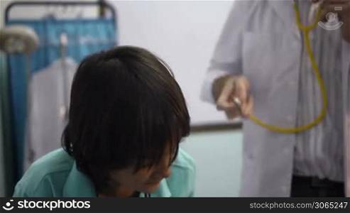 Friendly doctor working and visiting with stethoscope sick child coughing in private medical clinic. Rack focus