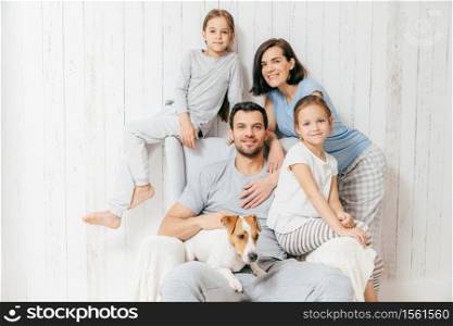 Friendly family of four memebers: cheerful European brunette female, her husband, two daughters and favourite pet, have good relationships, support each other. Affectionate parents with children