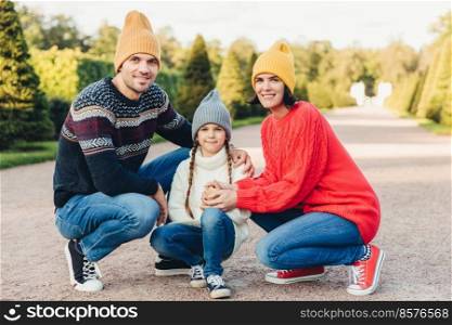 Friendly family wear knitted clothes, have walk together, admire splendid autumn weather. Affectionate young parents and their little cute daughter play together outdoor. Relationship concept
