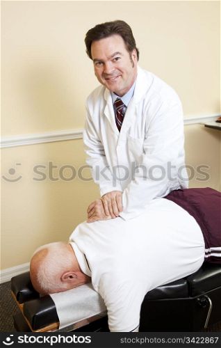 Friendly, smiling chiropractor adjusts an elderly patient&rsquo;s spine.