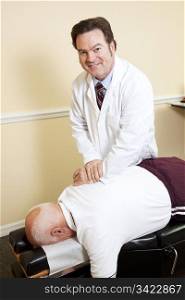 Friendly, smiling chiropractor adjusts an elderly patient&rsquo;s spine.