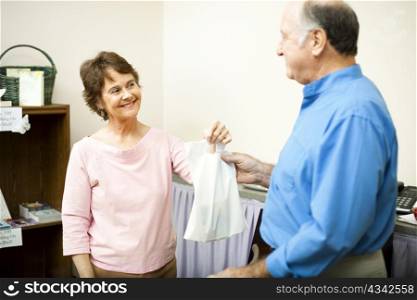 Friendly store clerk hands a customer his bag with a smile. Room for text