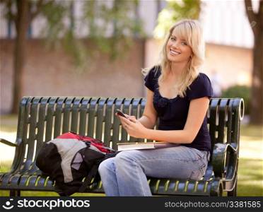 Friendly young female student sitting on a bench sending a text message