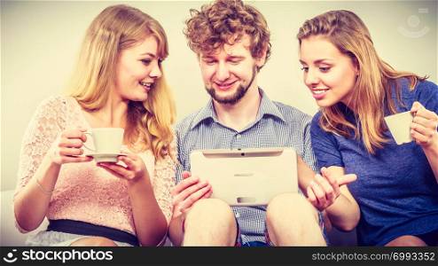 Friends browsing internet on tablet. Young people man guy and women girls relaxing at home.. Friends relaxing browsing internet on tablet.