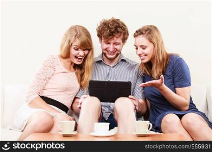 Friends browsing surfing internet on tablet. Young people man guy and women girls sitting on sofa relaxing at home.. Friends relaxing browsing internet on tablet.