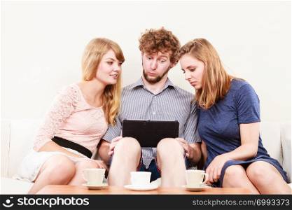 Friends browsing surfing internet on tablet. Young people man guy and women girls sitting on sofa relaxing at home.. Friends relaxing browsing internet on tablet.