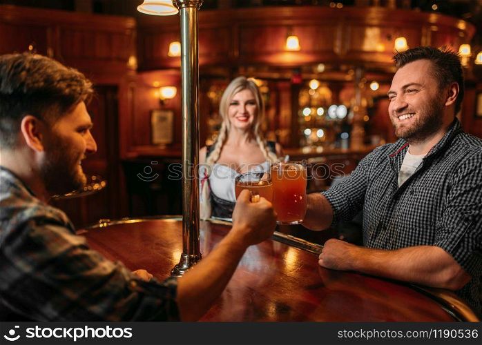 Friends clinking mugs in beer bar, waitress at the counter on background, oktoberfest holidays. Men with glasses having fun in pub, barmaid in traditional retro style. Friends clinking mugs, waitress on background
