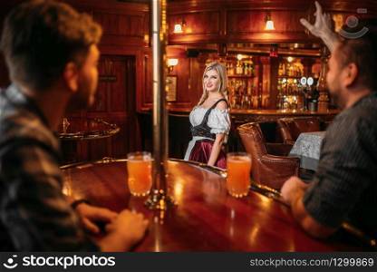 Friends clinking mugs in beer bar, waitress at the counter on background, oktoberfest holidays. Men with glasses having fun in pub, barmaid in traditional retro style. Friends clinking mugs, waitress on background