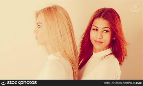 Friends dialogue between cultures. Blonde and mulatto girl together. Two young beautiful ladies, one has bright hair, second dark. Wearing white top.