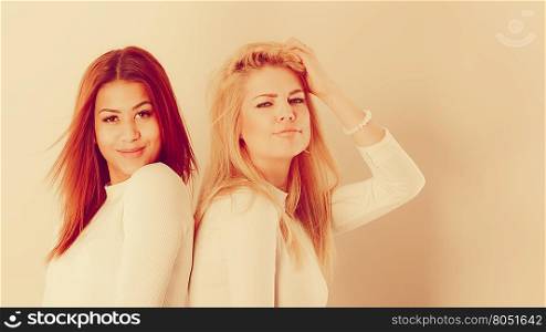 Friends dialogue between cultures. Blonde and mulatto girl together. Two young beautiful ladies, one has bright hair, second dark. Wearing white top.