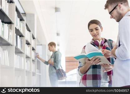 Friends discussing over book while student searching at shelf 