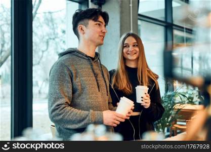 Friends doing shopping in a coffee shop. Young man and woman having chat while picking out the pastry, bakery&rsquo;s goods and hot drinks standing at counter in a coffee shop. People buying coffee and sweet snacks to go