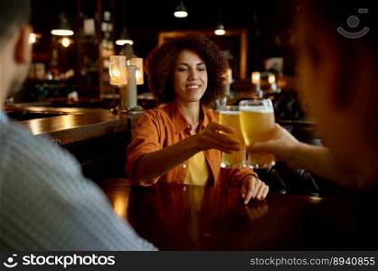 Friends drinking beer cheering glasses sitting at table in sport bar. Focus on happy smiling woman. Friendship, rest and recreation concept. Friends drinking beer cheering glasses sitting at table in sport bar