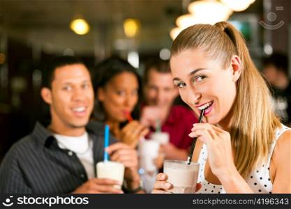 Friends drinking milkshakes in a bar and have lots of fun; focus on the woman in front