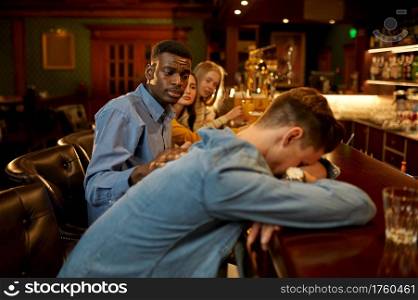 Friends drinks beer, man sleeps at the counter in bar. Group of people relax in pub, night lifestyle, friendship, event celebration. Friends drinks beer, man sleeps at counter in bar