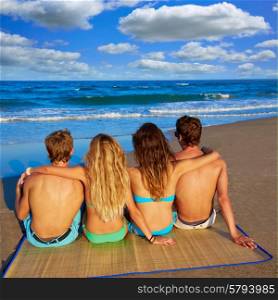 friends group couples sitting in beach sand rear view back looking to the sea