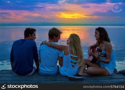 Friends group playing guitar in sunset pier at dusk beach happy