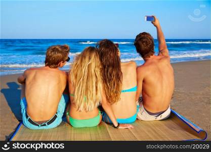 friends group selfie photo sitting in beach sand rear back view
