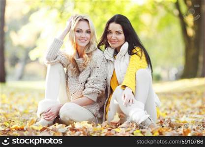 Friends in autumn park. Happy female friends sitting on ground in autumn park