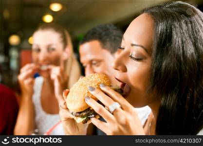 Friends - one couple is African American - eating hamburger and drinking soda in a fast food diner; focus on the woman in front