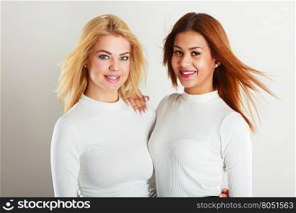 Friends people concept. Two young friends together. Girls have white top, standing next to each other. One lady has blonde hair, second dark ones.