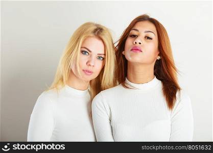 Friends people concept. Two young friends together. Girls have white top, standing next to each other. One lady has blonde hair, second dark ones.