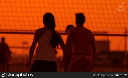 Friends playing volleyball on beach at sunset