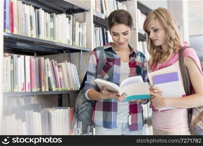 Friends reading book while standing at library