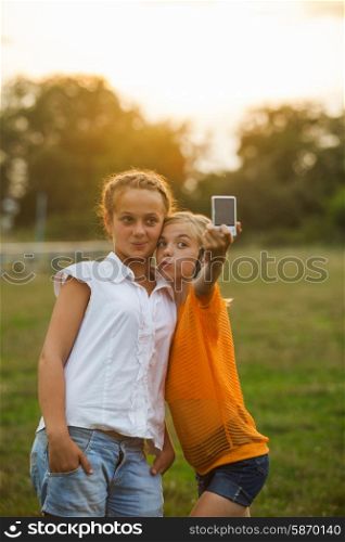 Friends taking a self portrait outdoor. Two girls makes selfie in the summer glow. Friends selfie