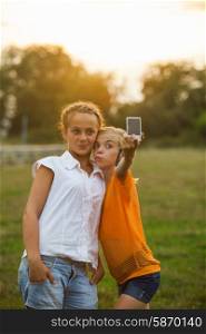 Friends taking a self portrait outdoor. Two girls makes selfie in the summer glow. Friends selfie