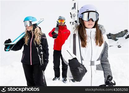 Friends wearing helmets and ski goggles holding skis, portrait