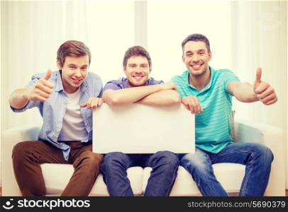 friendship and advertising concept - smiling male friends holding white blank board and showing thumbs up