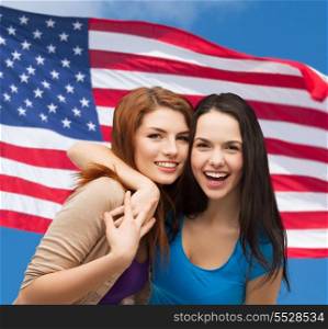 friendship and happy people concept - two laughing girls hugging over american flag background