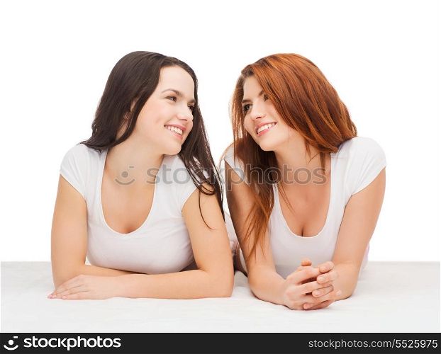 friendship and happy people concept - two laughing girls in white t-shirt looking at each other