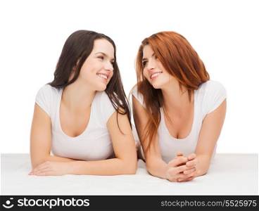 friendship and happy people concept - two laughing girls in white t-shirt looking at each other