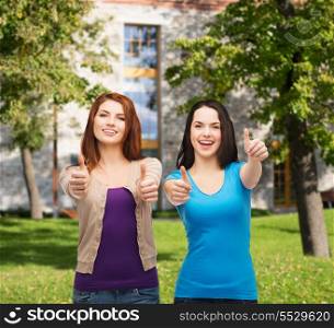 friendship and happy people concept - two smiling girls showing thumbs up