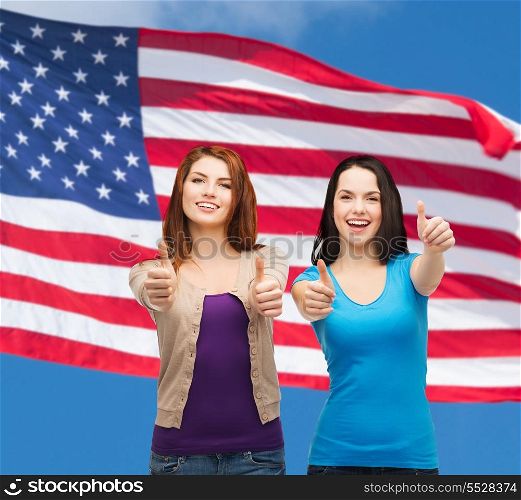 friendship and happy people concept - two smiling girls showing thumbs up over american flag background