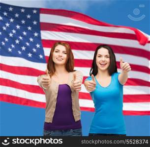 friendship and happy people concept - two smiling girls showing thumbs up over american flag background