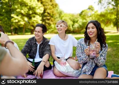 friendship and leisure concept - group of happy friends with non alcoholic drinks and food at picnic in summer park. happy friends with drinks at picnic in summer park