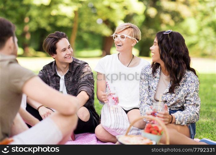 friendship and leisure concept - group of happy friends with non alcoholic drinks and food at picnic in summer park. happy friends with drinks at summer picnic