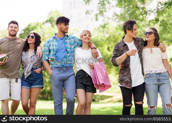 friendship and leisure concept - group of happy friends with picnic blanket and watermelon walking at summer park. happy friends with picnic blanket at summer park