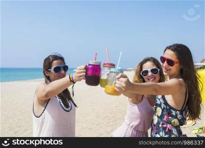 friendship and leisure concept - group of happy young women or female friends toasting non alcoholic drinks on summer beach