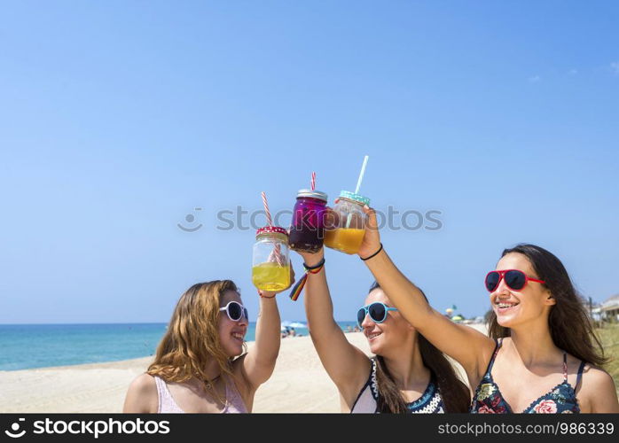 friendship and leisure concept - group of happy young women or female friends toasting non alcoholic drinks on summer beach