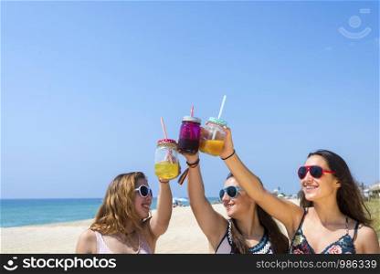 friendship and leisure concept - group of happy young women or female friends toasting non alcoholic drinks on summer beach