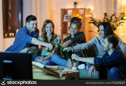 friendship, and leisure concept - happy friends with non-alcoholic drinks and pizza watching tv at home in evening. friends with drinks and pizza watching tv at home