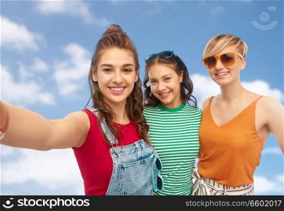 friendship and people concept - group of happy female smiling friends in sunglasses taking selfie over blue sky and clouds background. happy female friends in sunglasses taking selfie