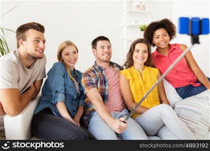 friendship, and people concept - group of happy friends taking picture with smartphone and selfie stick at home